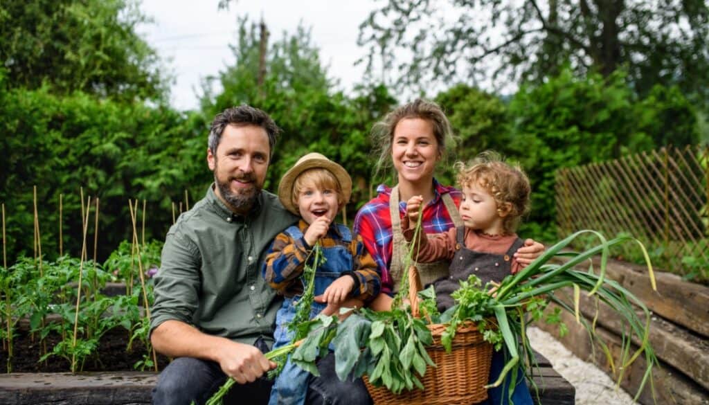 Family standing in garden holding vegetables, homesteading